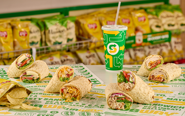 Four Subway wraps on Subway sandwich paper next to chips and a cup