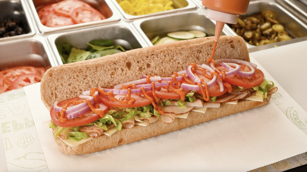 Subway Creamy Sriracha sauce drizzling on footlong sandwich behind the counter